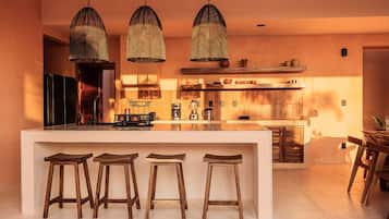 Una cocina moderna con una isla central, taburetes de madera, lámparas colgantes y una zona de bar de madera.