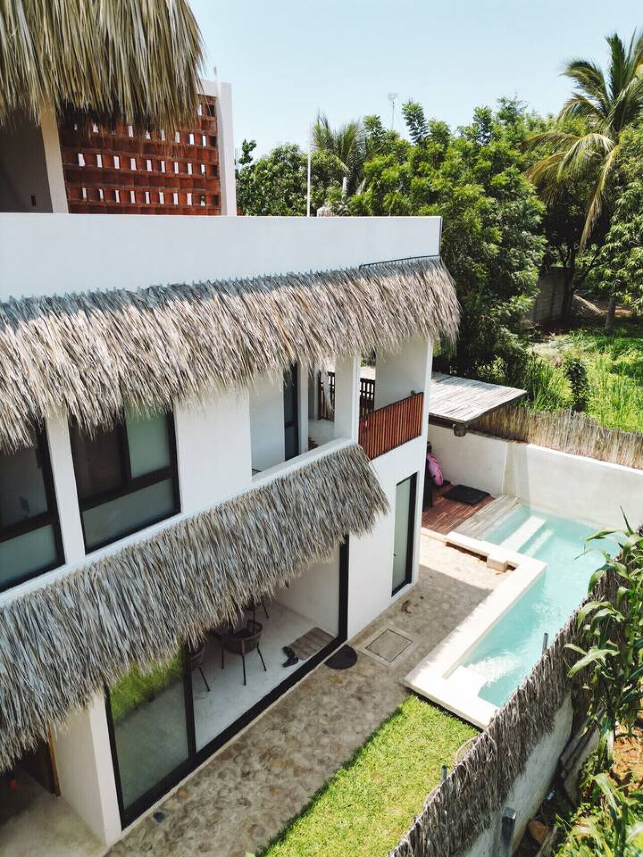 A modern house with a pool, thatched roof, and lush greenery.