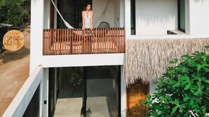 A two-story building with a thatched roof, a balcony with wooden railings, and a clear sky. - Alberca privada, starlink, AC, a 5 min de la punta (Puerto Escondido)