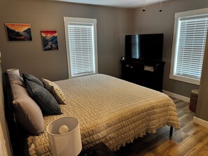 Un dormitorio con cama, televisor y dos ventanas con persianas.