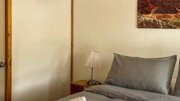 A bedroom with a bed, a nightstand, a lamp, a painting, and a wooden ceiling beam.