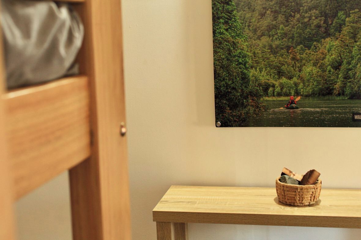 Un armario de madera con puerta cerrada, un cuadro colgado en la pared de un kayakista en un río y una pequeña mesa de madera con una cesta.