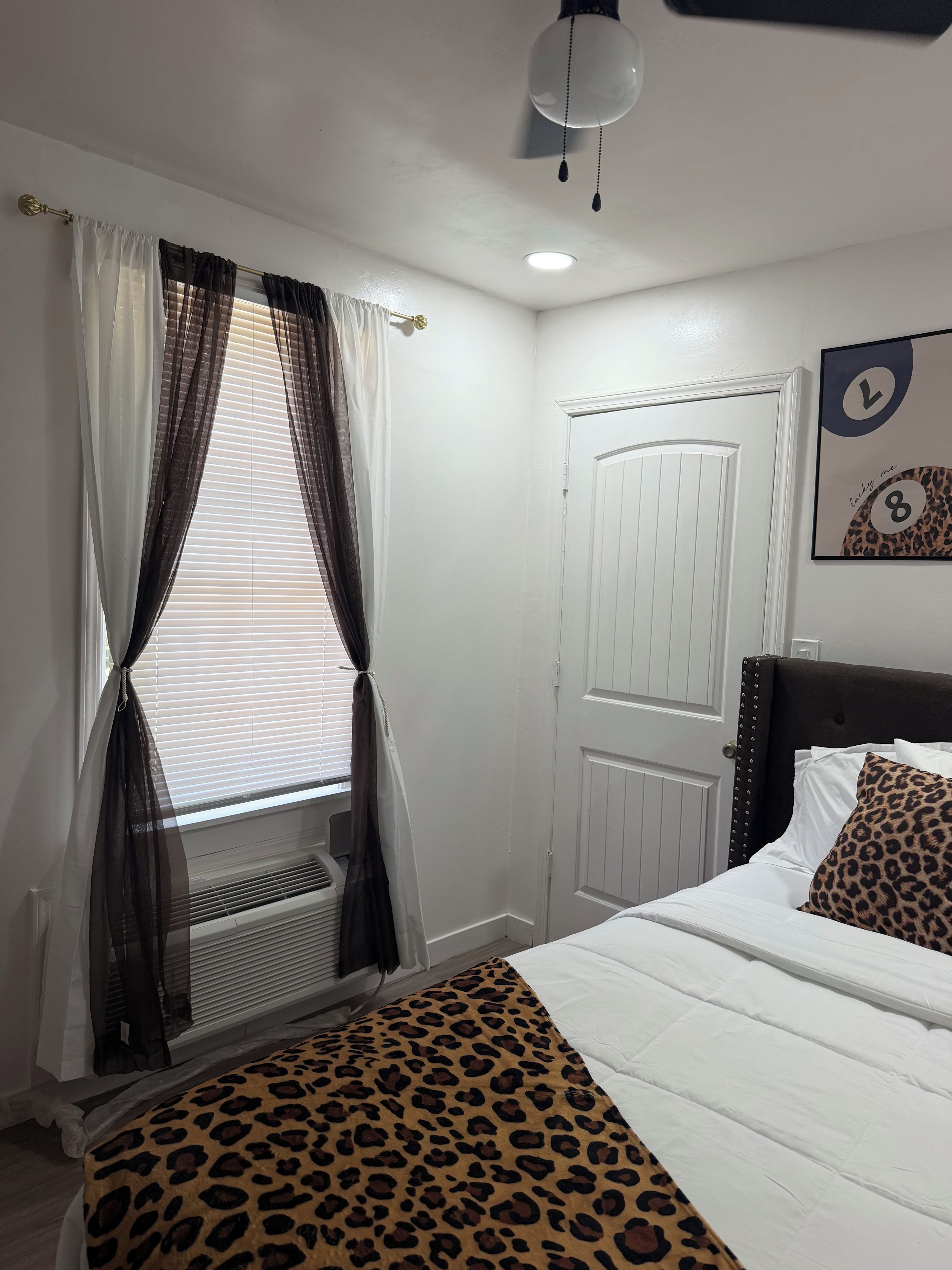 Un dormitorio con cama, ventana con cortinas, puerta y un reloj de pared.