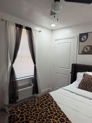 A bedroom with a bed, a window with curtains, a door, and a wall clock.