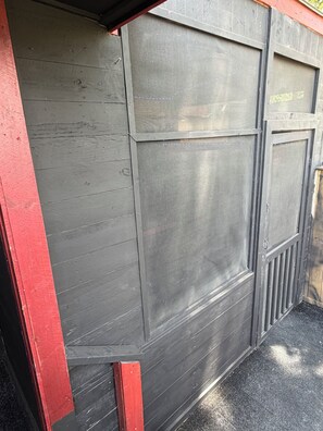 Una reja metálica gris con una malla, un poste pintado de rojo y un suelo texturizado negro.