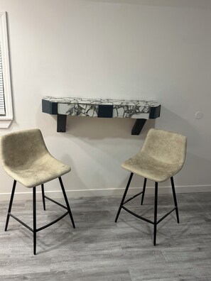 Una habitación con una mesa de diseño de mármol, dos sillas con patas negras y una pared blanca lisa.