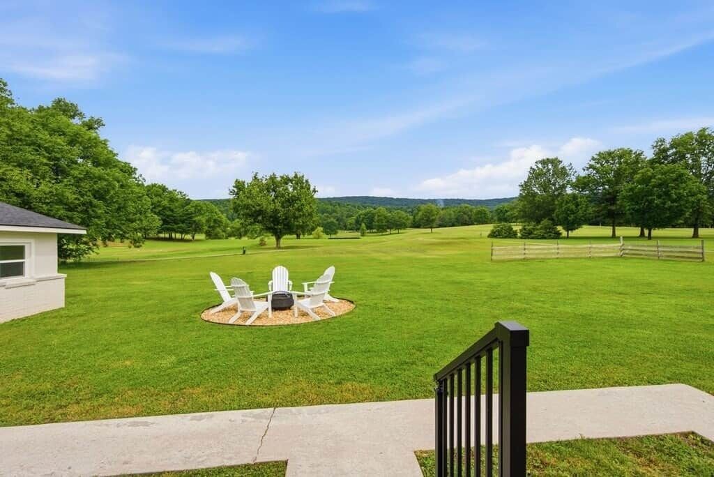A grassy yard with a patio table and chairs, a wooden fence, and a house in the background.