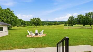 A grassy yard with a patio table and chairs, a wooden fence, and a house in the background.