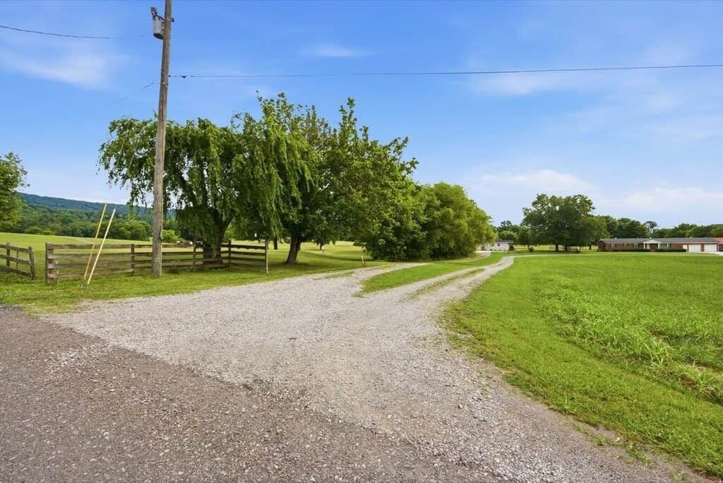 A rural road with a gravel path, wooden fence, and trees.