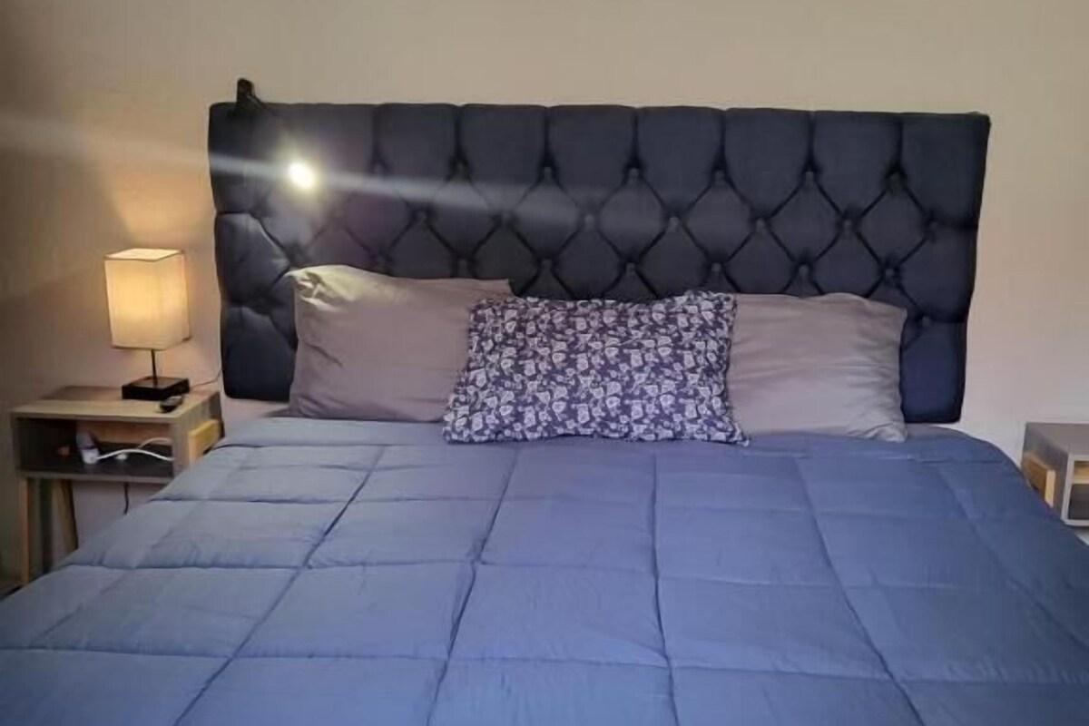 Un lit avec une tête de lit capitonnée, une courtepointe bleue et un coussin à motifs.