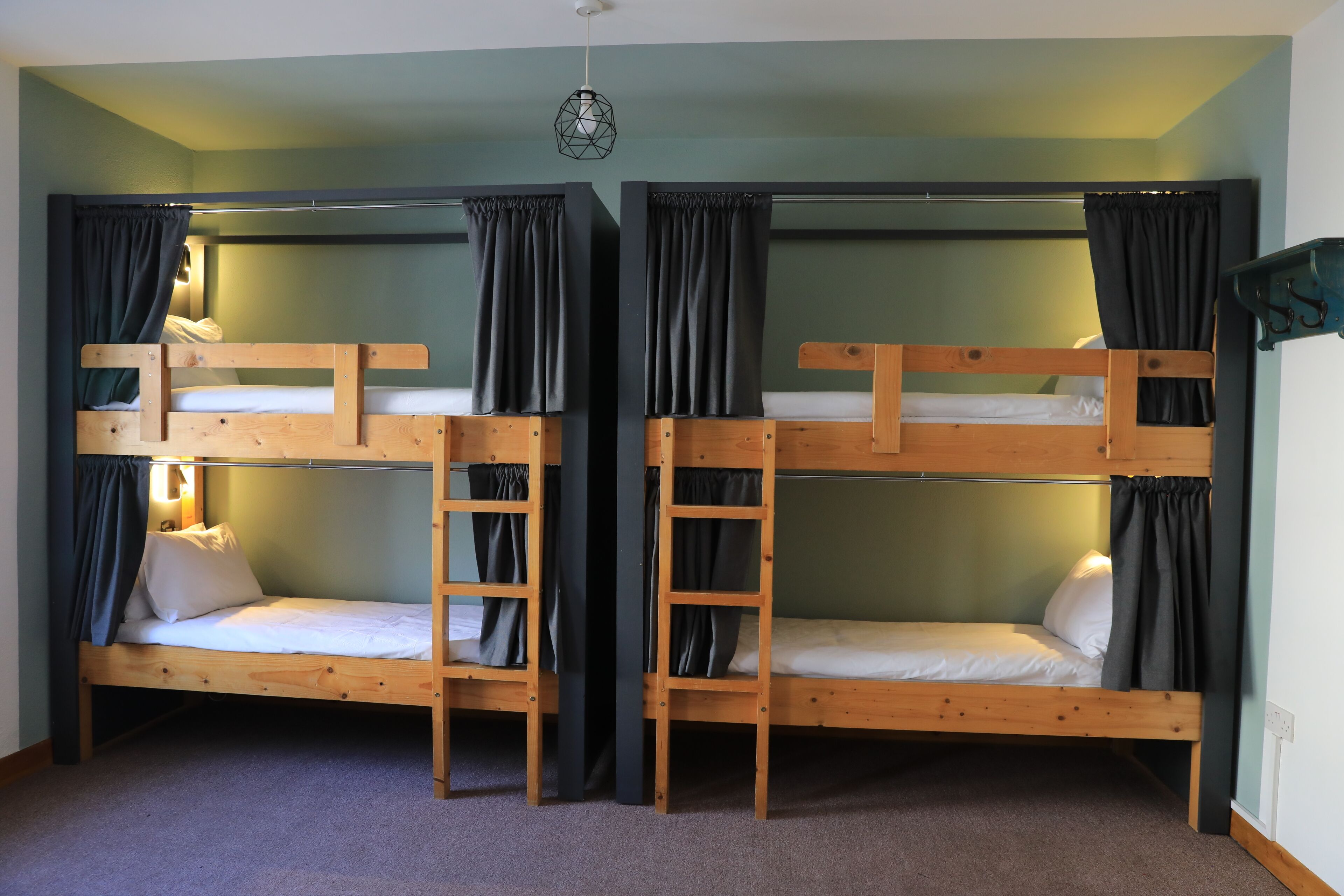 A room with two bunk beds, each with a ladder, and a hanging light fixture.