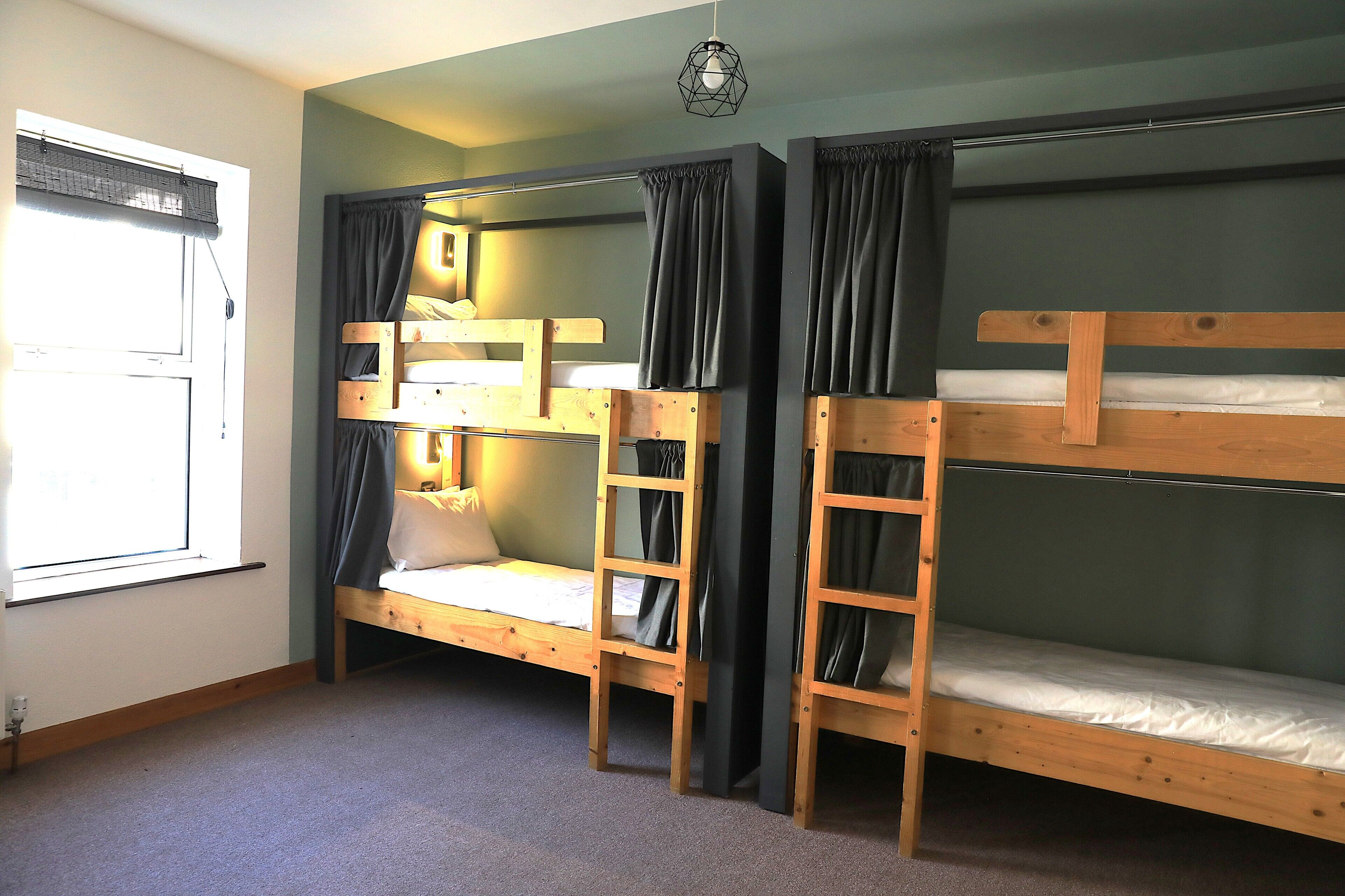 A room with bunk beds, a window with blinds, and a hanging light fixture.
