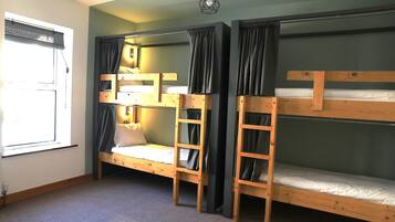 A room with bunk beds, a window with blinds, and a hanging light fixture.