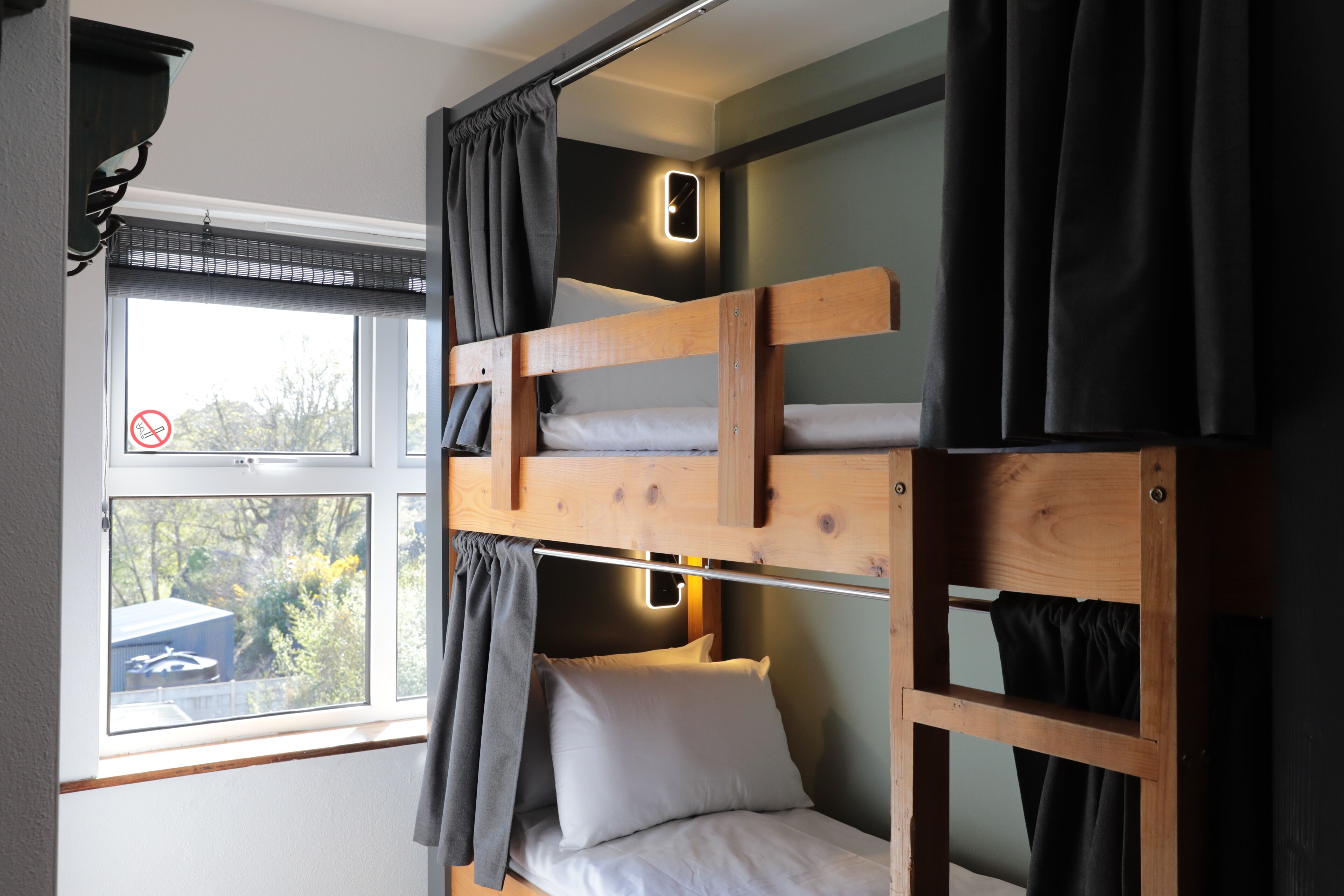 A bunk bed with a window, curtains, and a wall-mounted light fixture.