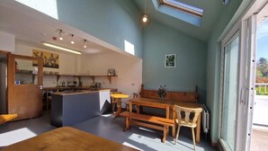 A room with a wooden table, benches, a small island with a sink, and a large window.