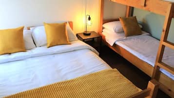 A room with two beds, each with white bedding and yellow pillows, a bedside table with a lamp, and a wooden ladder attached to the bed on the right.