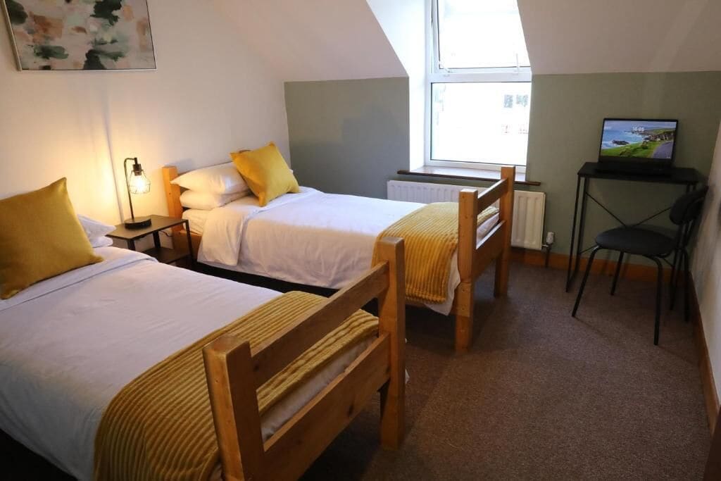 A bedroom with two beds, a desk with a computer, a chair, and a window.