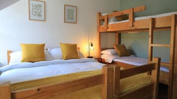 Habitación con literas de madera, ropa de cama blanca y una manta amarilla.