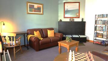 A living room with a brown sofa, a wooden chair, a coffee table, a chessboard, a bookshelf, and a fireplace.