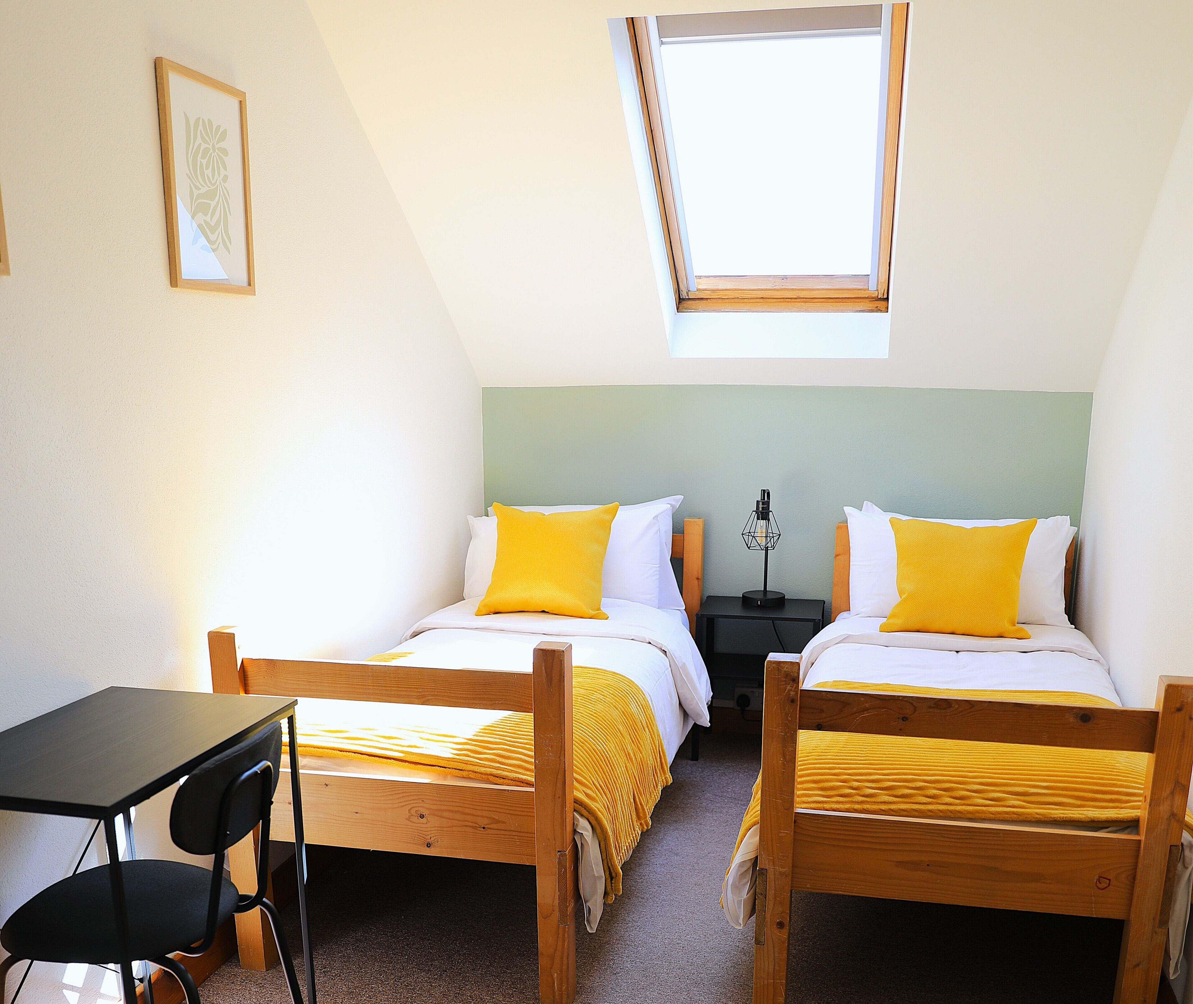 A room with two wooden beds, a desk, a chair, and a skylight.