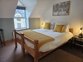 A bedroom with a sloped ceiling, a bed with white bedding and yellow pillows, a wooden headboard, a bedside table with a lamp, and a painting on the wall.