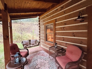 A log cabin with a porch, wicker furniture, a table, and a lantern. - Historic Schoolhouse/Log Cabin - minutes to the beautiful South Branch River! (Romney)