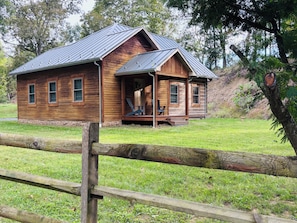 A wooden cabin with a porch, a small deck, and a fenced yard. - Historic Schoolhouse/Log Cabin - minutes to the beautiful South Branch River! (Romney)