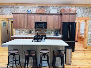A kitchen with wooden cabinets, a central island with stools, a refrigerator, and a microwave.