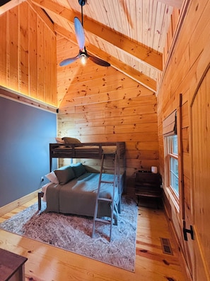 A cozy cabin room with a bunk bed, a ceiling fan, and a window. - Historic Schoolhouse/Log Cabin - minutes to the beautiful South Branch River! (Romney)