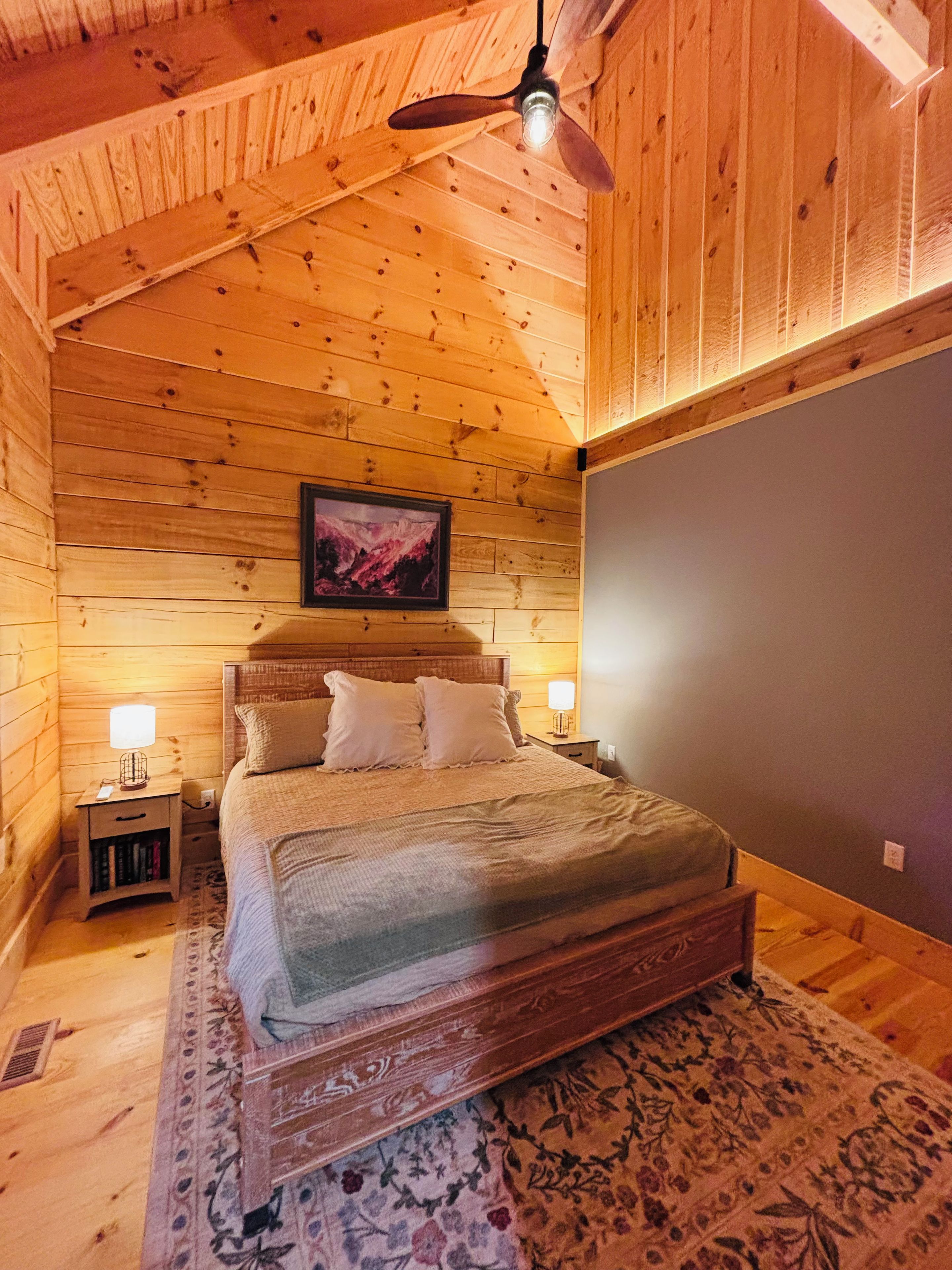 A wooden cabin bedroom with a bed, nightstands, a ceiling fan, and a framed picture on the wall.