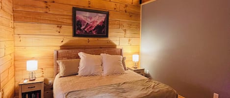 A wooden cabin bedroom with a bed, nightstands, a ceiling fan, and a framed picture on the wall.