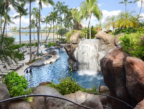 Une piscine de villégiature avec une cascade, entourée de palmiers et de chaises longues.