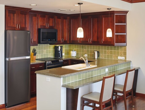 Une cuisine dotée de meubles en bois, d’appareils électroménagers en acier inoxydable, d’un dosseret de carrelage vert et de luminaires suspendus.