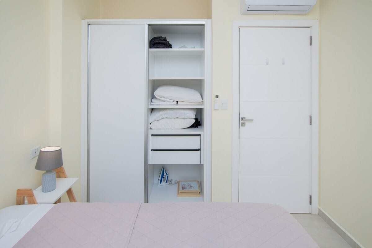 Une chambre à coucher comprenant un lit, une armoire, une table de chevet avec une lampe et une porte équipée d’un appareil de climatisation.