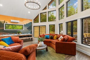 A modern interior with large windows, a dining area, and a seating area with orange sofas. - Pickleball Court, Hot Tub, Theatre, Secret Room! (Albrightsville)
