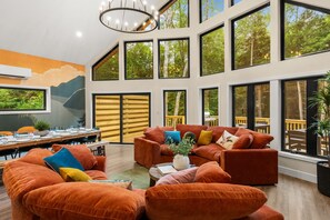 A spacious room with large windows, a dining area, and a cozy seating area with orange sofas. - Pickleball Court, Hot Tub, Theatre, Secret Room! (Albrightsville)