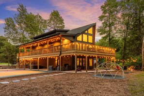 A two-story wooden cabin with a balcony, outdoor seating, and string lights. - Pickleball Court, Hot Tub, Theatre, Secret Room! (Albrightsville)