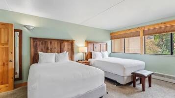 Habitación de hotel con dos camas, cabecera de madera, un pequeño banco y ventana con vistas.