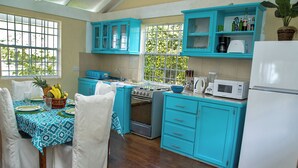 Een keuken met blauwgroene kastjes, een fornuis, een magnetron, en een eethoek met een tafel gedekt voor twee personen.