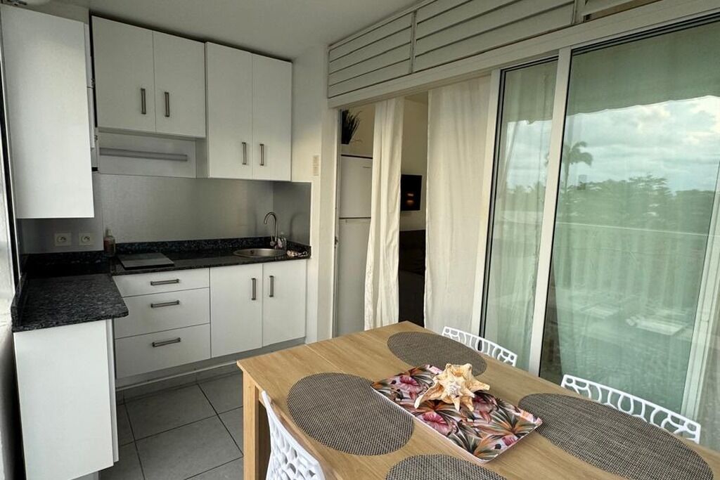 Una cocina funcional con armarios blancos, encimera negra y comedor con mesa de madera y protectores de mesa tejidos.