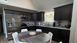 A modern kitchen with dark cabinets, a stainless steel refrigerator, a microwave, and a coffee maker. - Hollerwood Duo :Two Homes, One Epic Stay (Stanton)