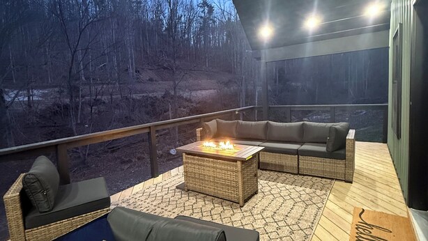 An outdoor deck with wicker furniture, a fire pit, and a view of a forested area. - Hollerwood Duo :Two Homes, One Epic Stay (Stanton)