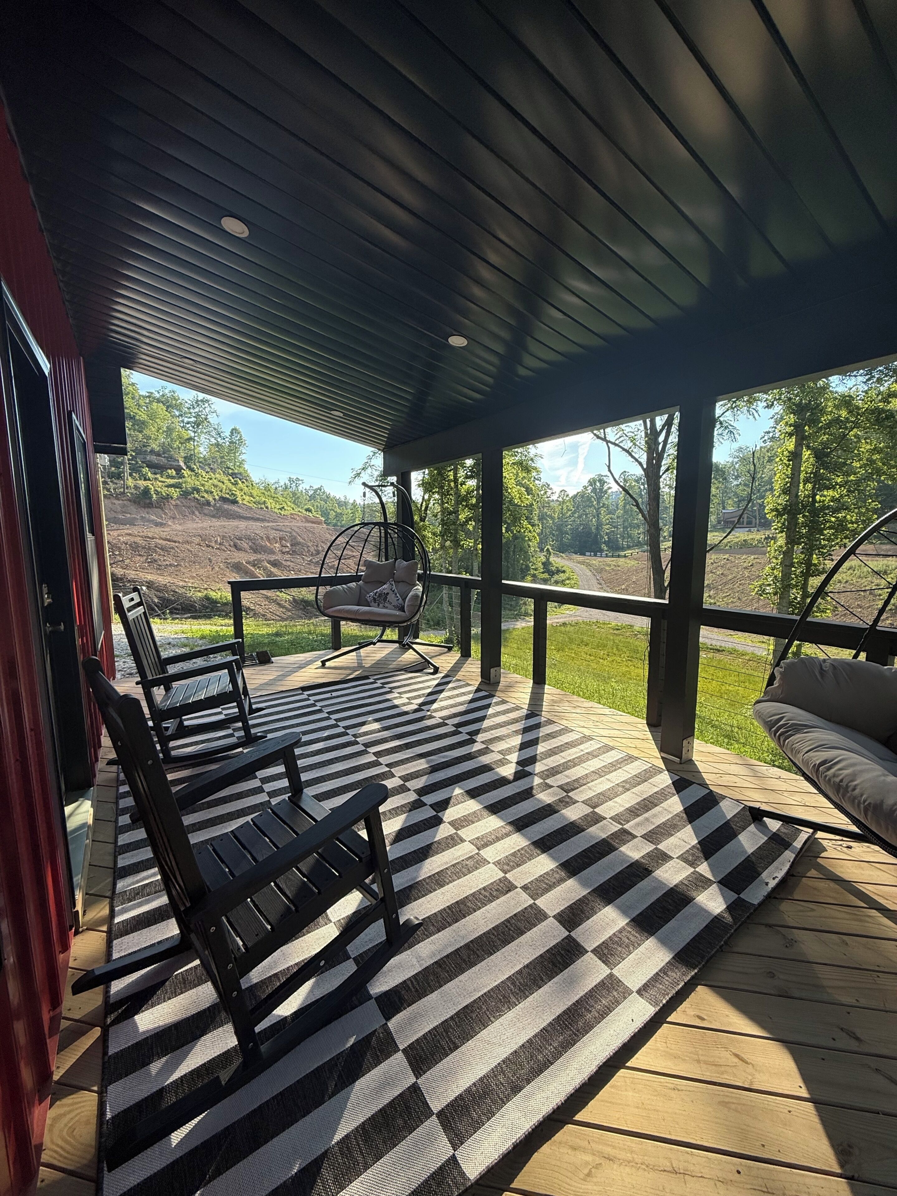 En overdækket terrasse med et ternet tæppe, træbænke og en hængekøjsstol.