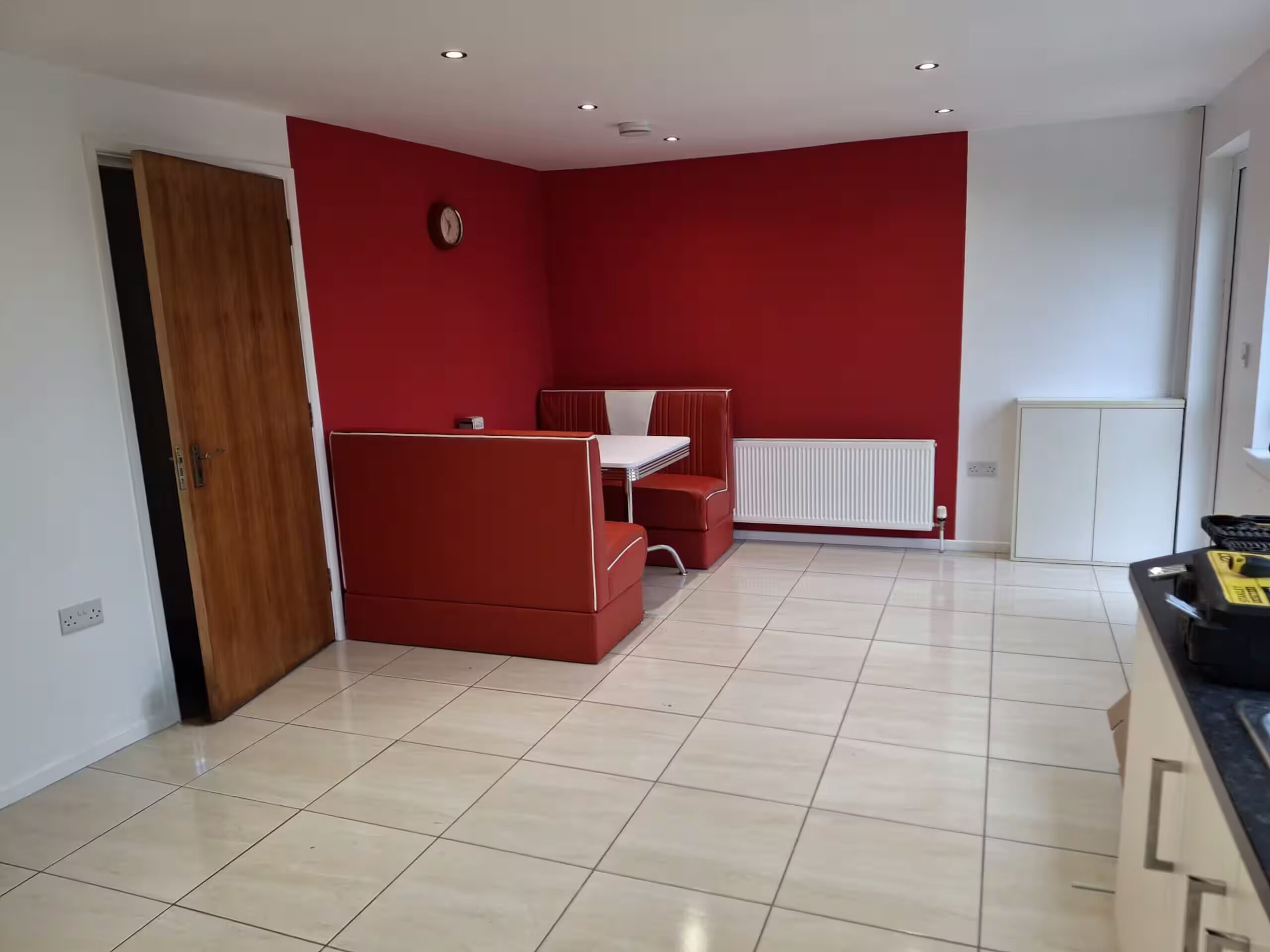 Una stanza con una parete rossa, un termosifone bianco, una porta in legno e un pavimento piastrellato.