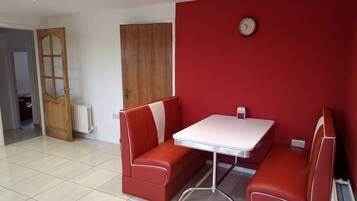 A room with a red wall, a wooden door, a white radiator, and a table with two red chairs.