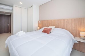 Hotellihuone, jossa on suuri sänky, puinen pääty, yöpöytä lampun kanssa ja vaatekaappi.