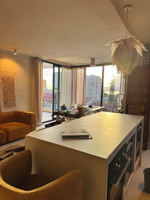Eine moderne Küche mit einer großen Kochinsel, einem Essbereich mit einer Couch und Blick auf Gebäude durch große Fenster.