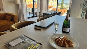 Ein Zimmer mit einem Laptop, einer Bollinger Champagnerflasche, einem Champagnerglas, einem Croissant auf einem Teller und einer Zeitschrift auf einem Tisch.