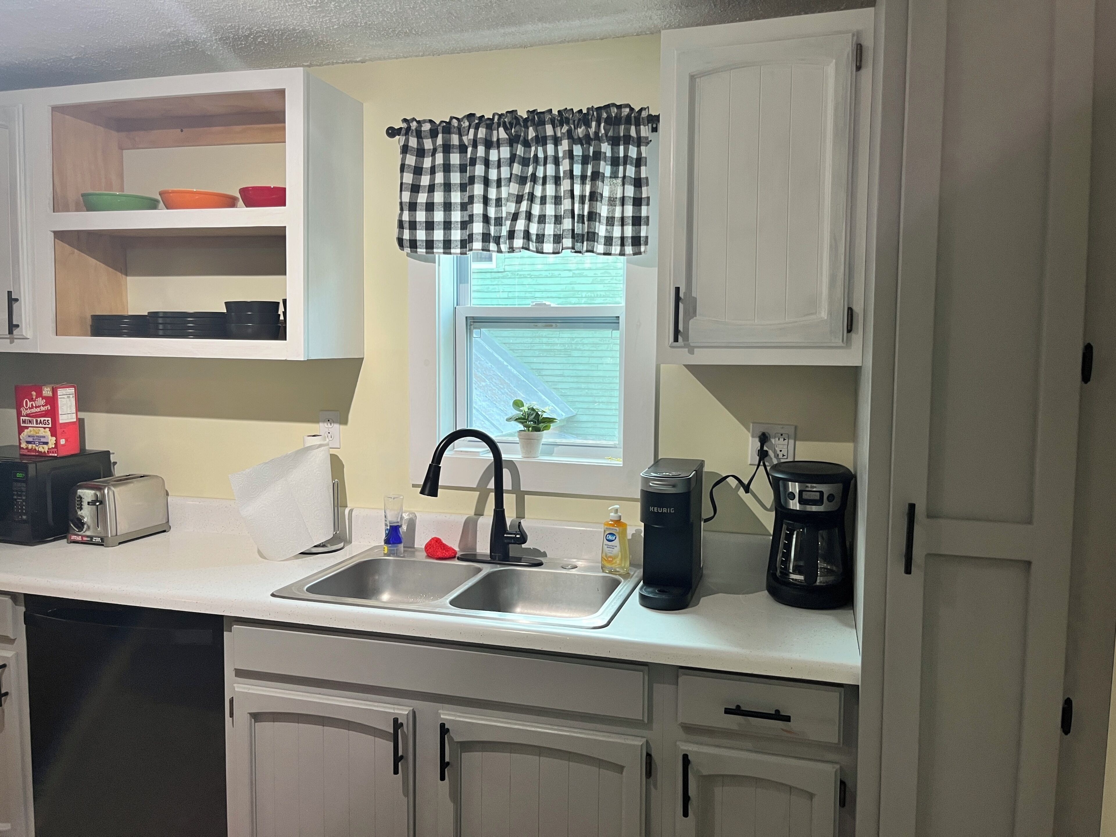 A kitchen with white cabinets, a sink, a toaster, a kettle, and a coffee maker.