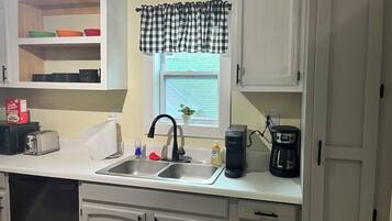 A kitchen with white cabinets, a sink, a toaster, a kettle, and a coffee maker.